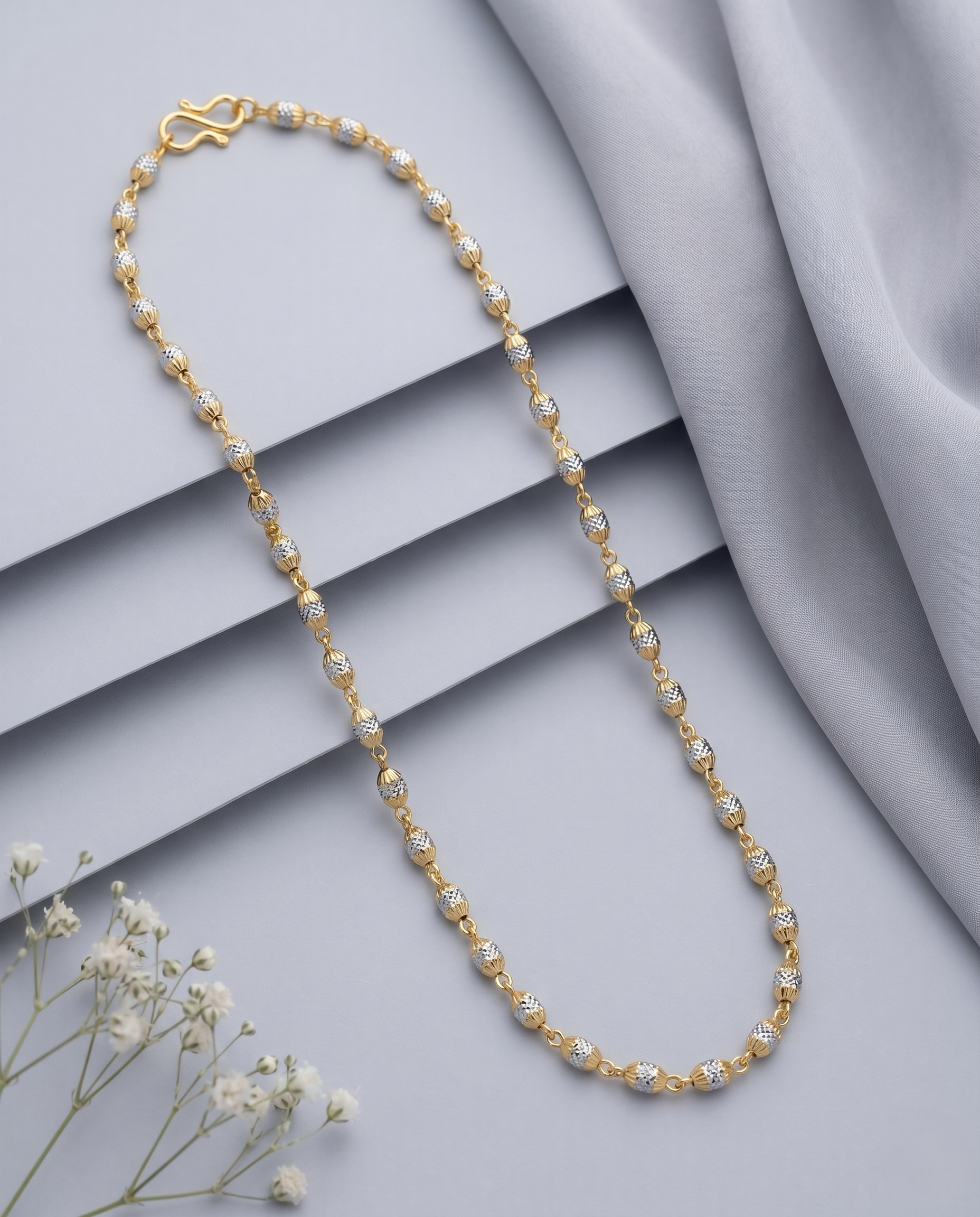 Gold necklace with small pearls on a gray surface with white flowers