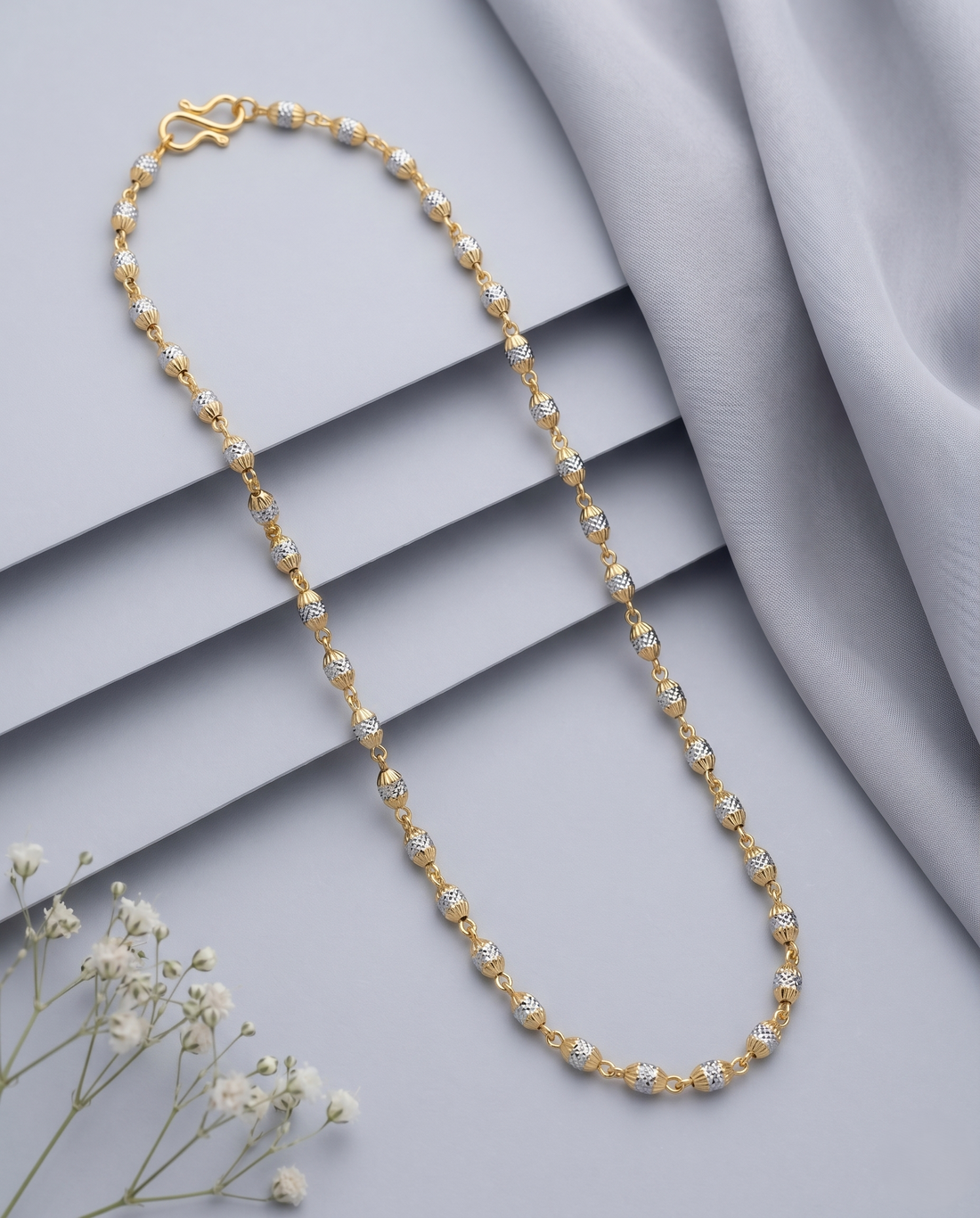 Gold necklace with small pearls on a gray surface with white flowers
