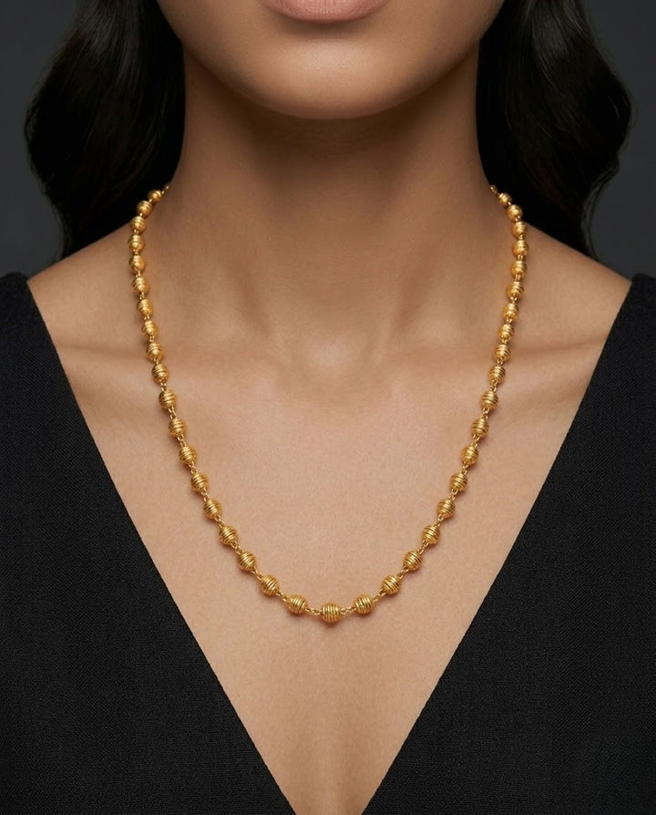 Gold necklace worn by a model against a dark background