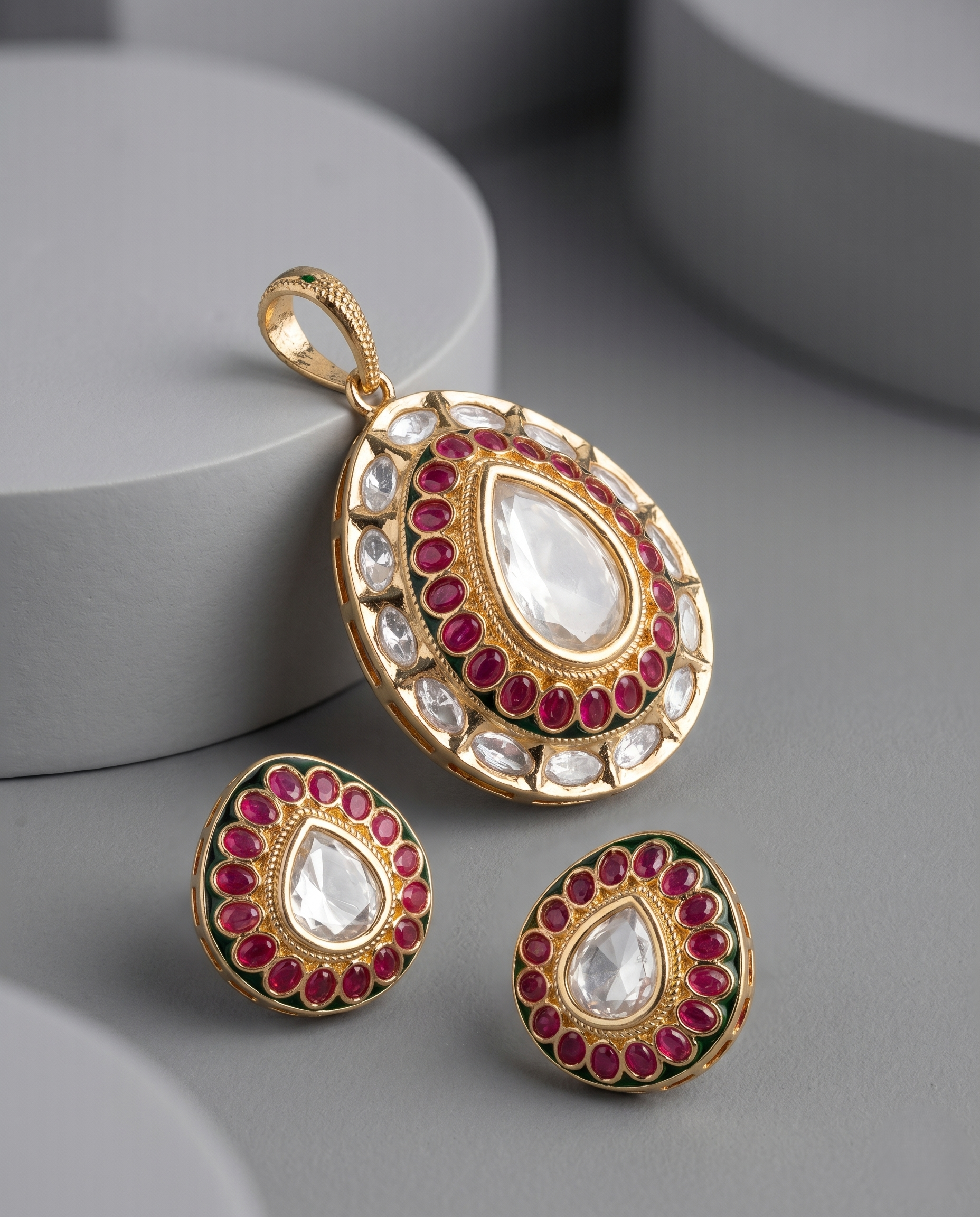 Gold pendant and earrings with red and white stones on a gray surface