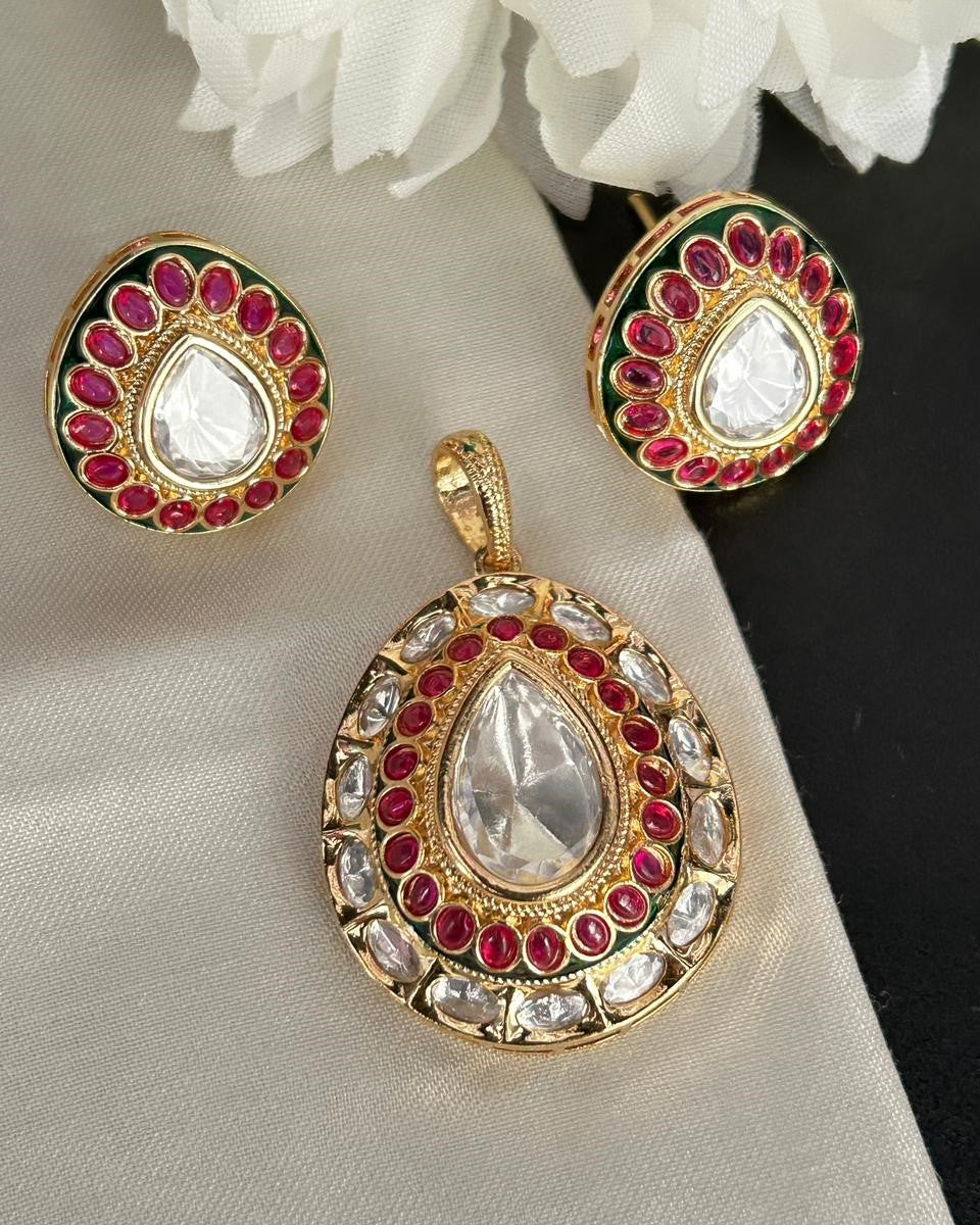 Gold pendant and earrings with red and white stones on a light fabric background