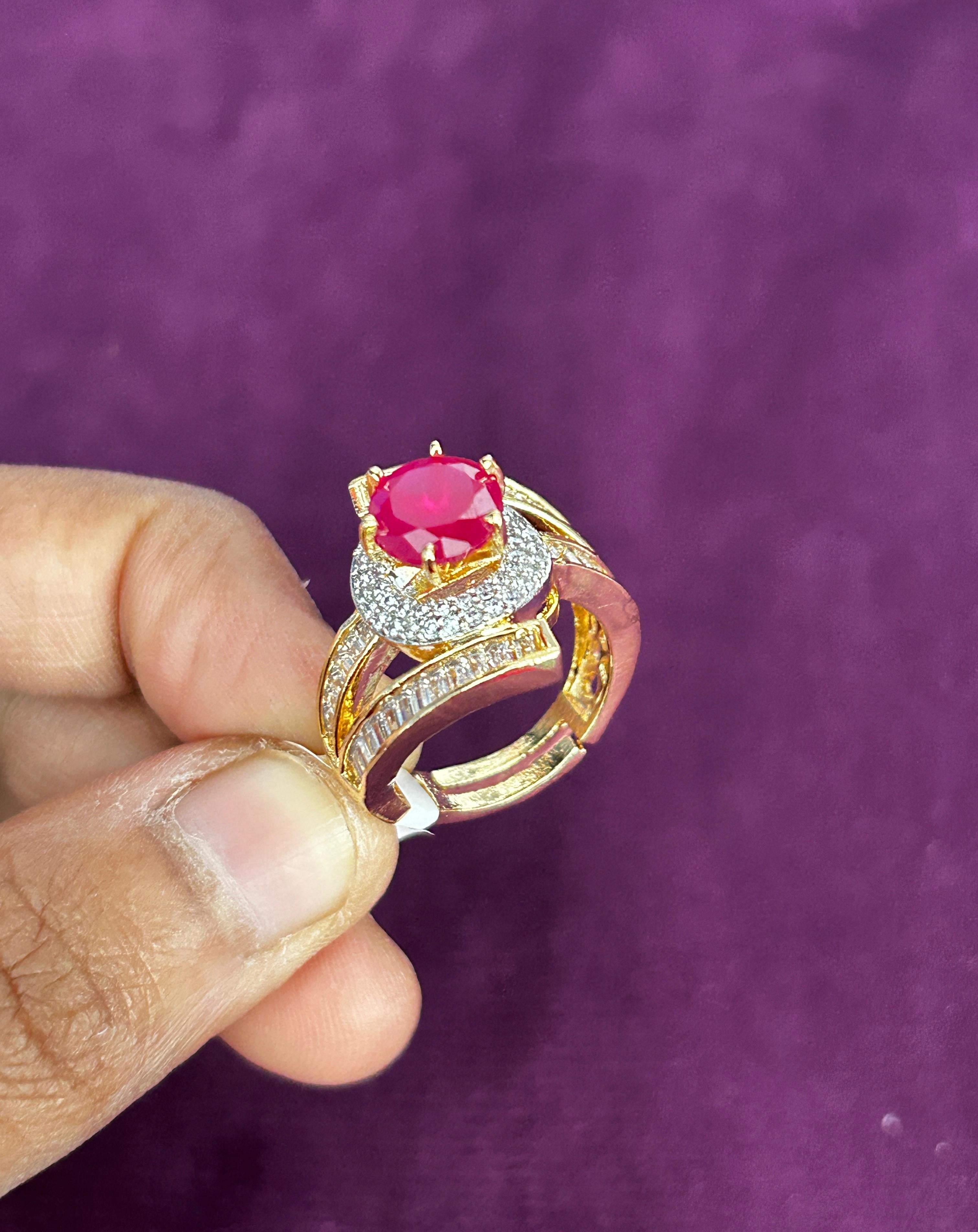 Gold ring with a red gemstone held by a hand against a purple background
