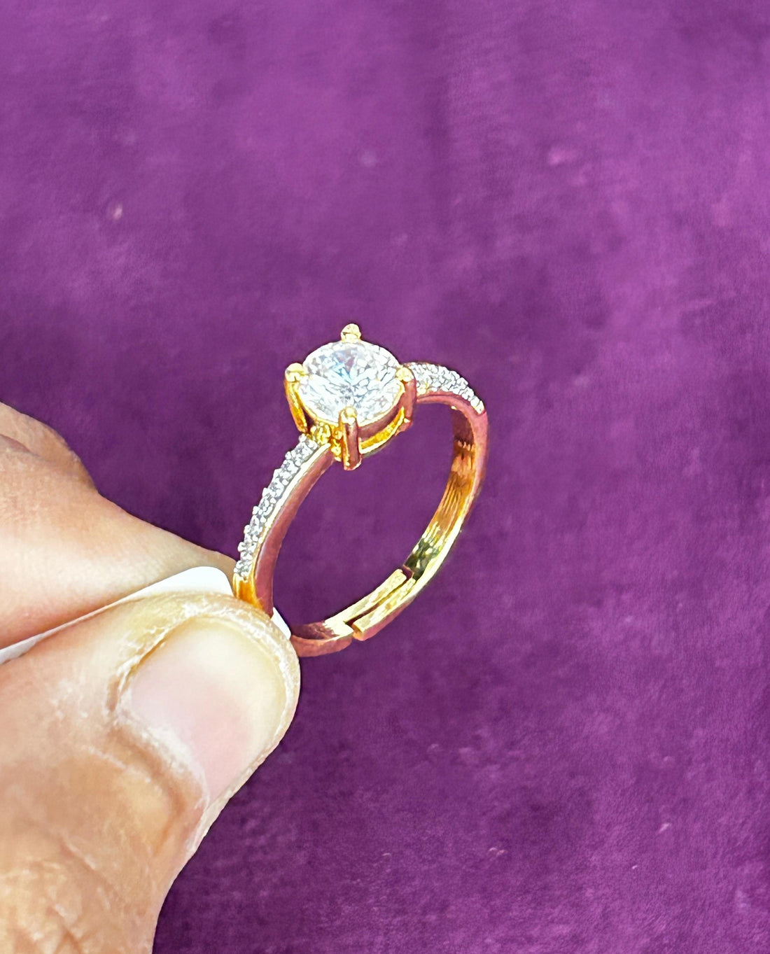 Gold ring with a diamond held by a hand against a purple background