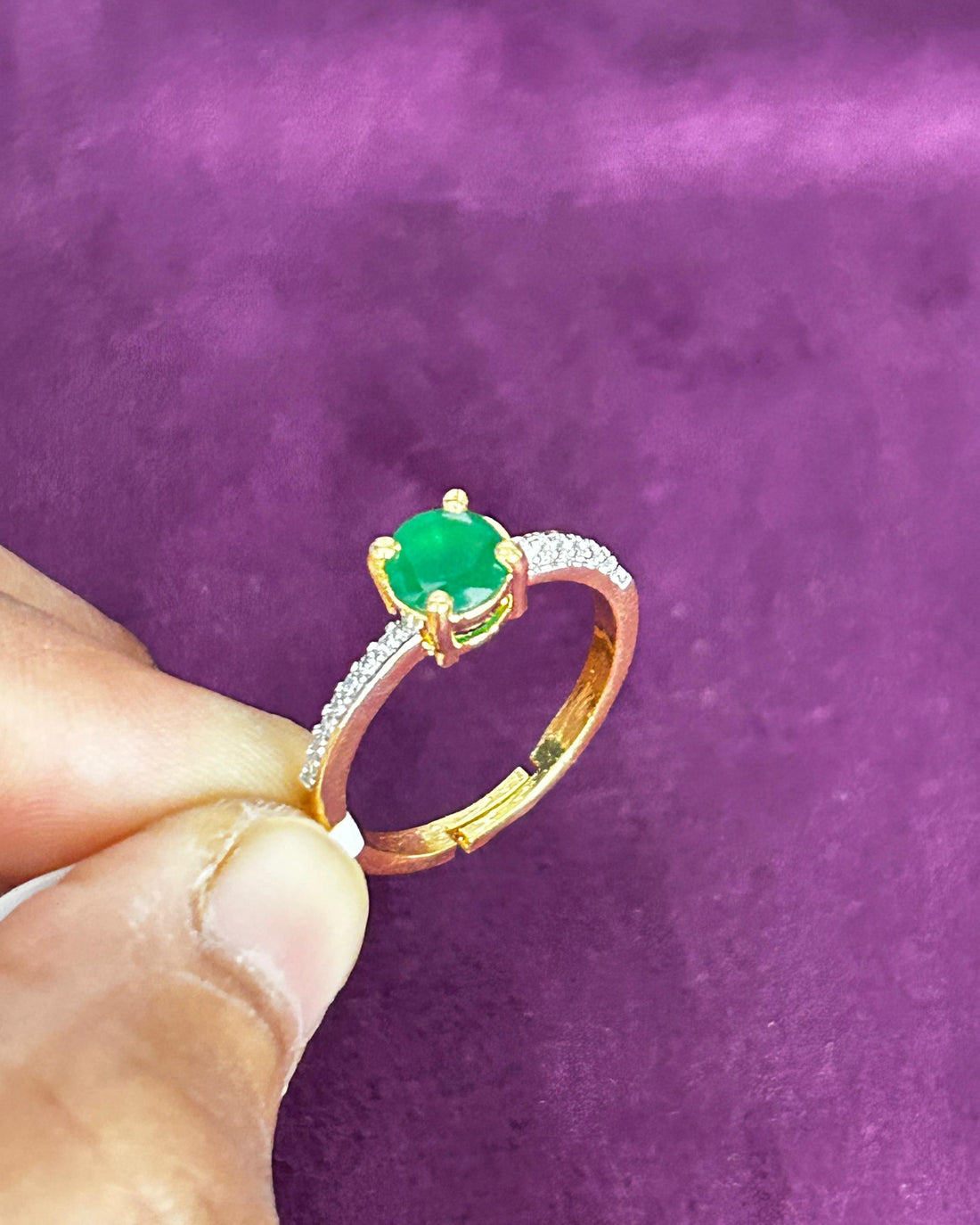 Gold ring with a green gemstone held by a hand against a purple background