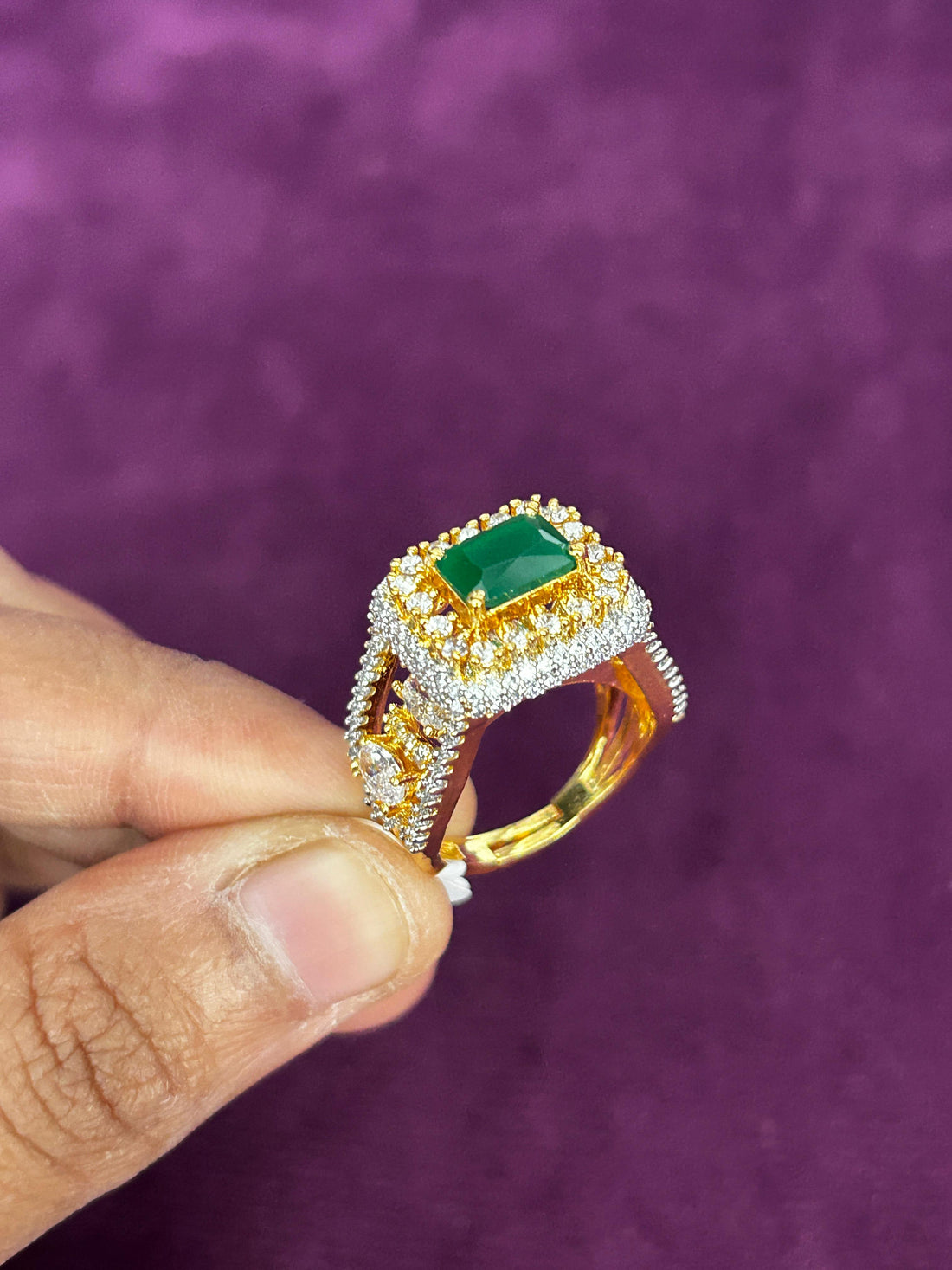 Gold ring with a green gemstone held by a hand against a purple background