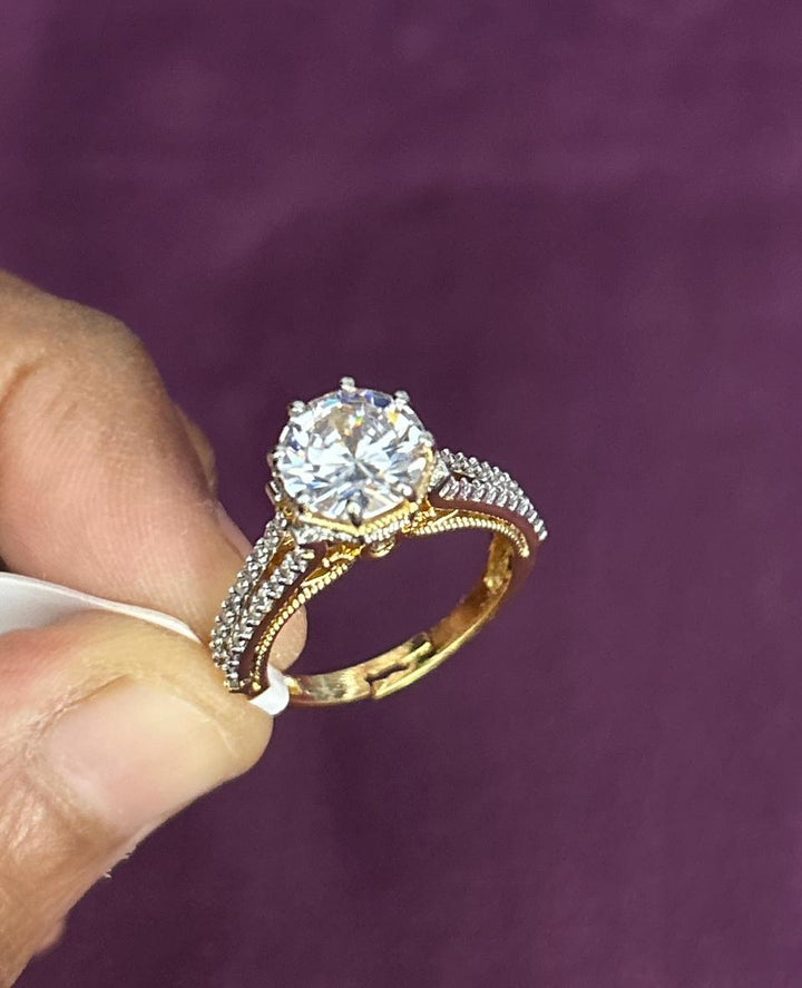 Gold ring with a large diamond held by a hand against a purple background