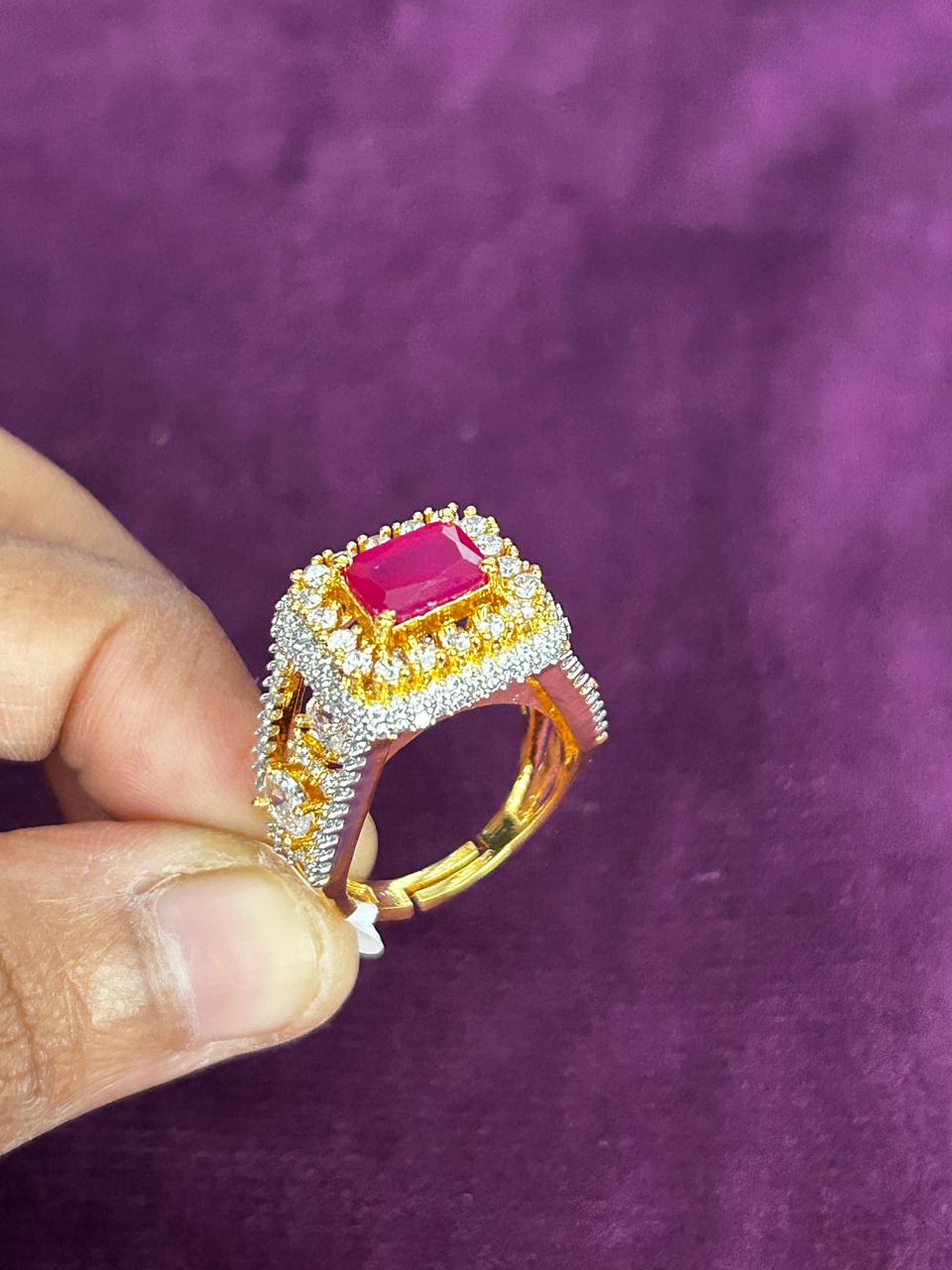 Gold ring with a pink gemstone held by a hand against a purple background