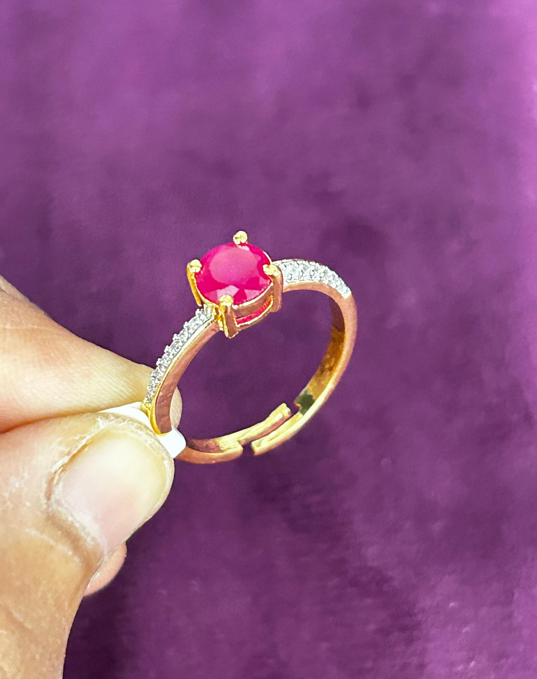 Gold ring with a red gemstone held by a hand against a purple background