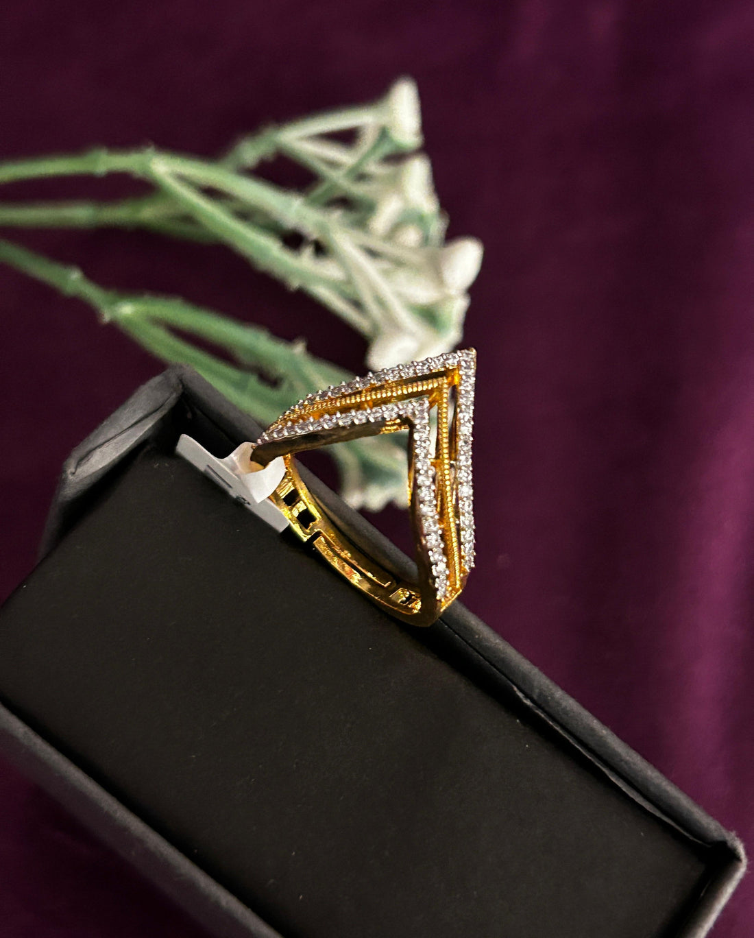 Gold ring with diamond accents on a black box against a purple background