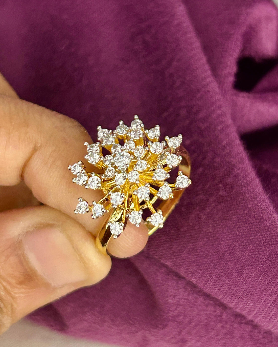 Gold ring with diamonds held by a hand against a purple fabric background
