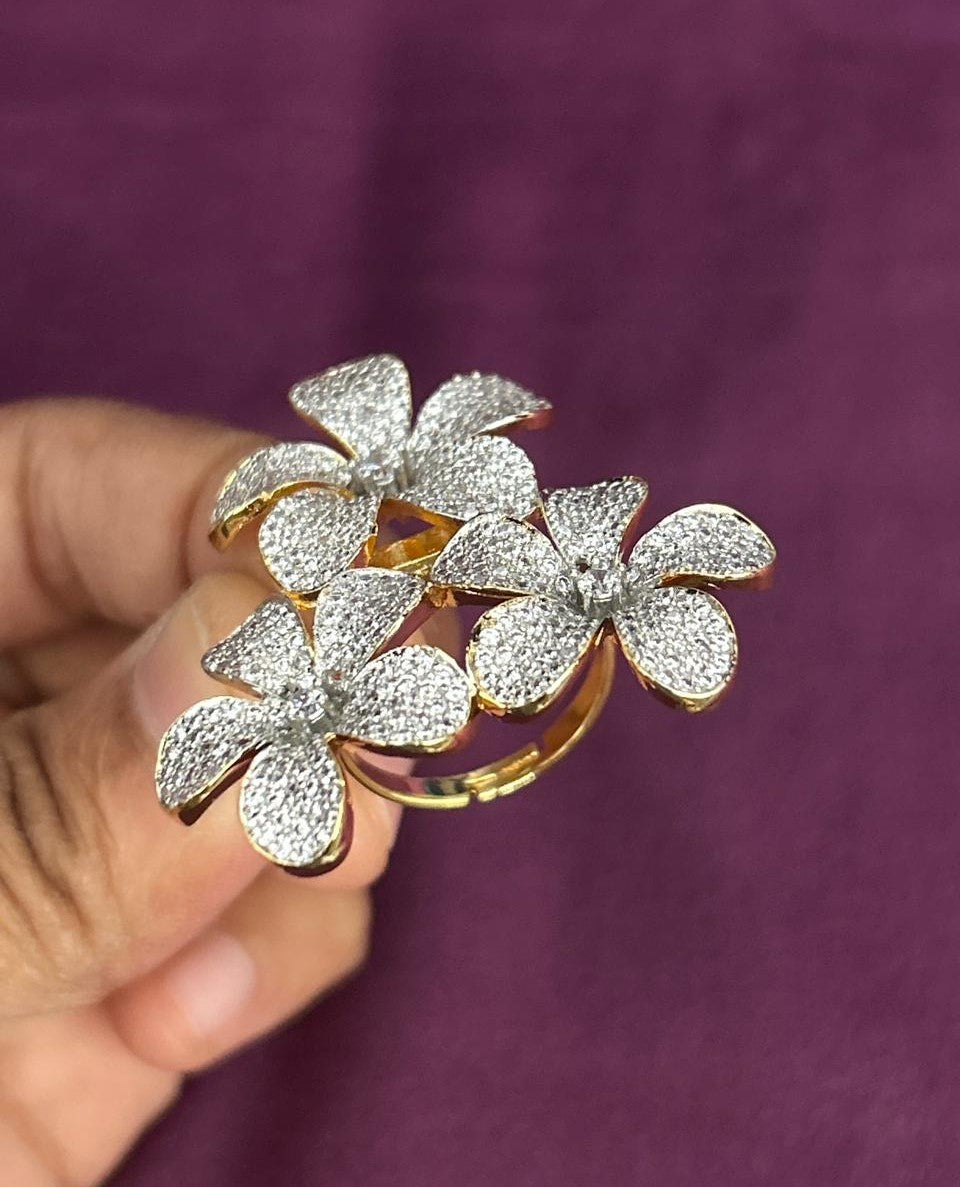 Gold ring with floral design held by a hand against a purple background
