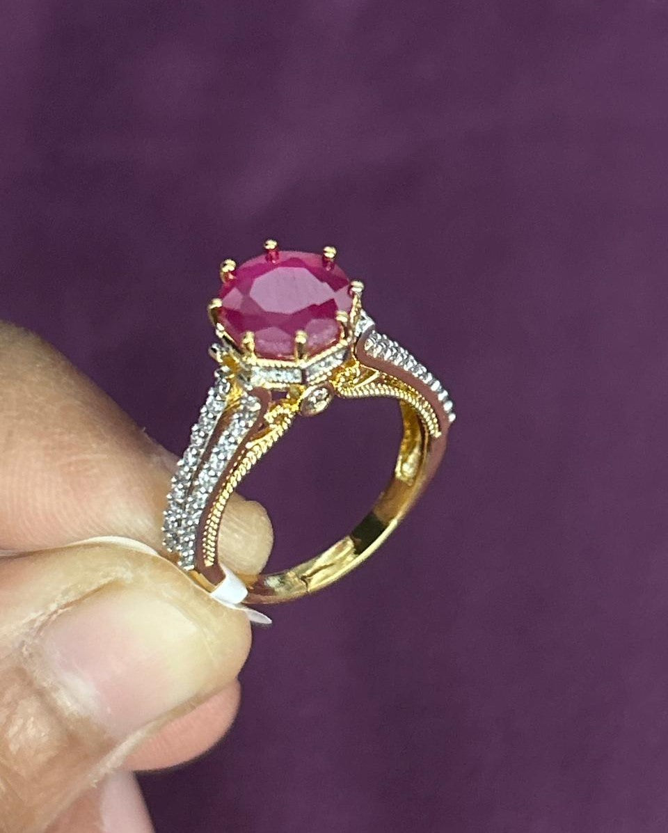 Gold ring with a red gemstone held by a hand against a purple background