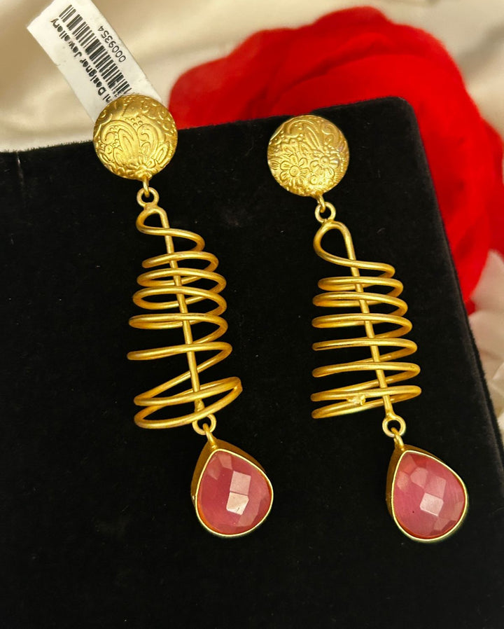 Gold spiral earrings with pink drops on a black stand
