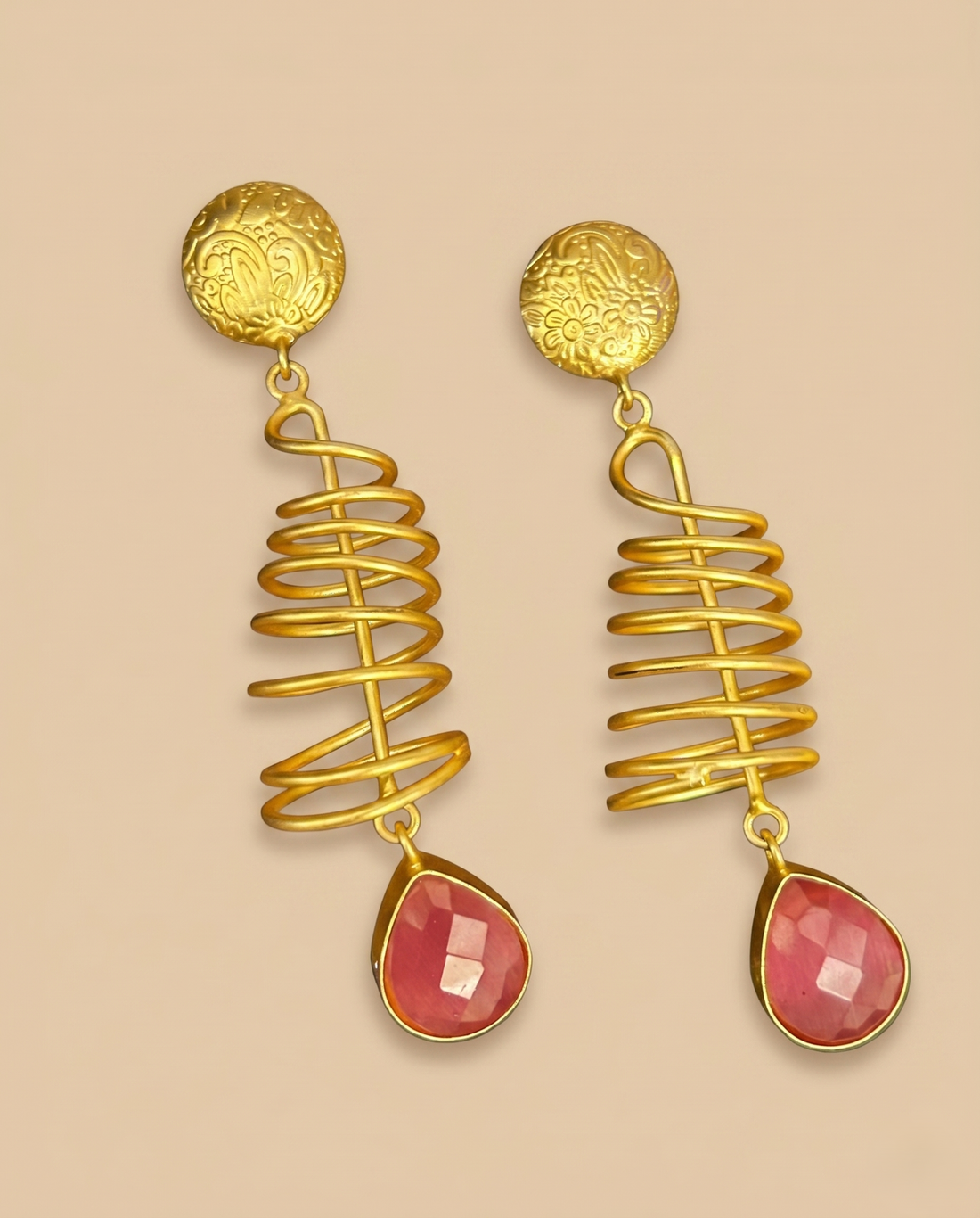 Gold spiral earrings with pink stones on a beige background