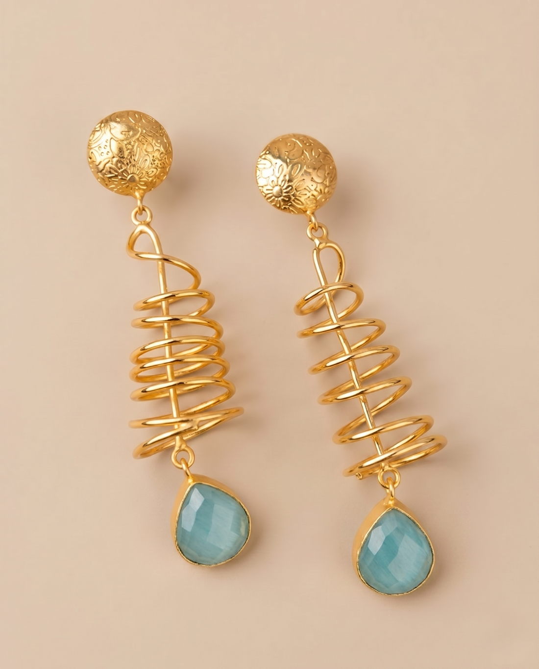 Gold spiral earrings with turquoise drops on a beige background