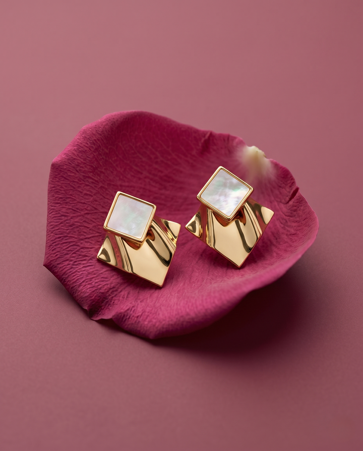 Gold square earrings on a pink flower petal against a matching background