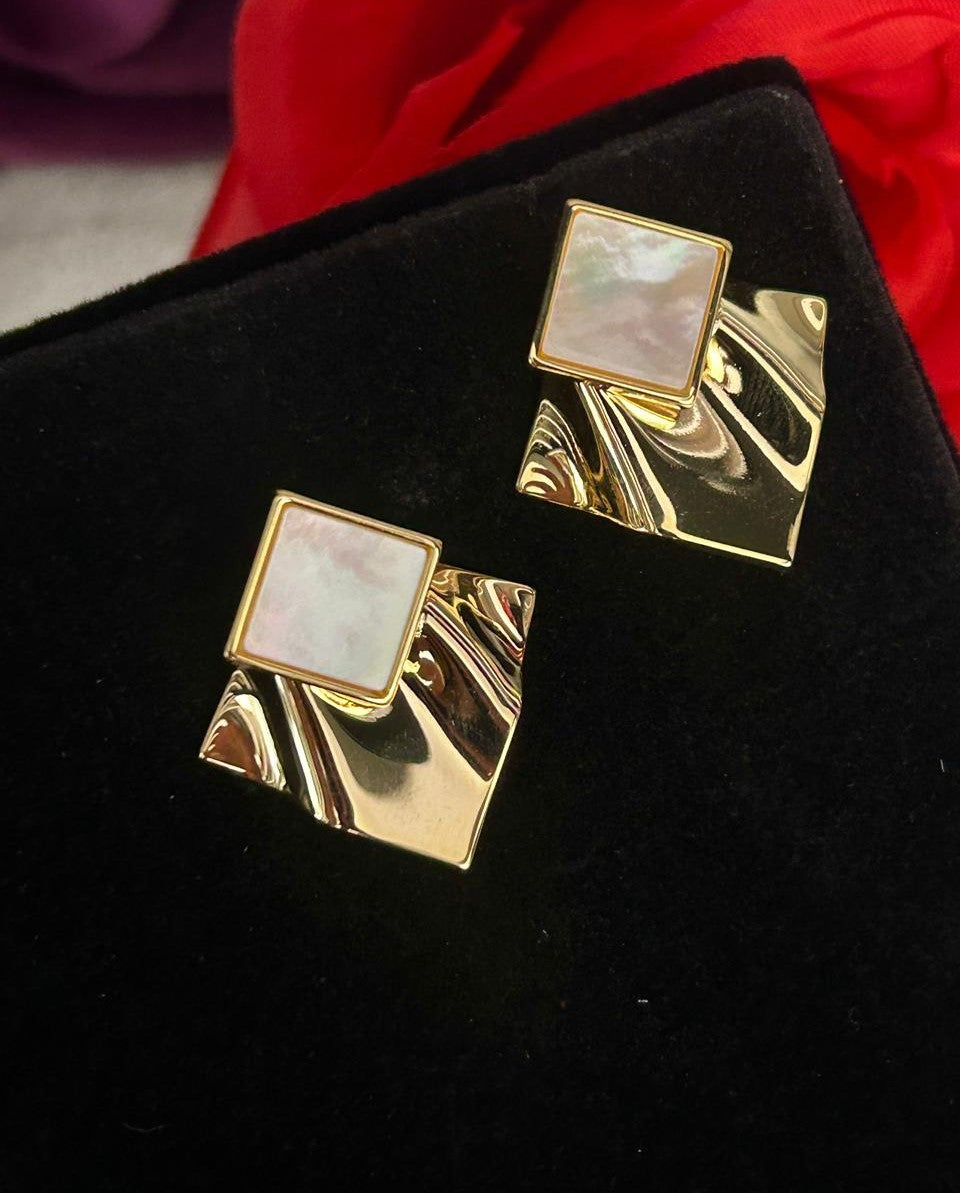 Gold square earrings with a central stone on a black background