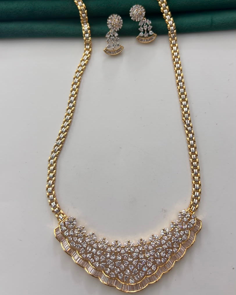 Gold statement necklace and matching stud earrings with clear rhinestone embellishments, displayed on a white surface with a dark green fabric backdrop.
