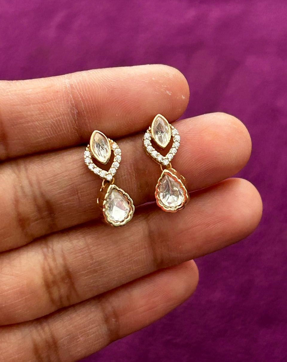 Gold teardrop earrings held between fingers against a purple background