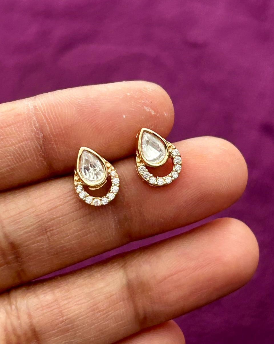 Gold teardrop earrings with clear stones held between fingers against a purple background