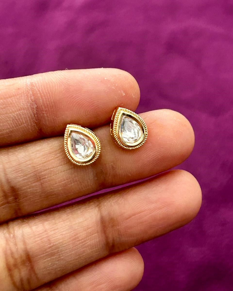 Gold teardrop earrings held between fingers against a purple background