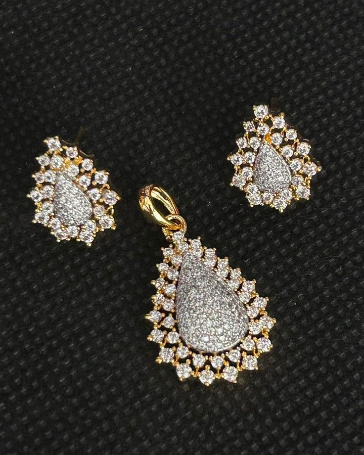 Gold teardrop pendant and matching stud earrings set with pavé diamonds on a textured black background.