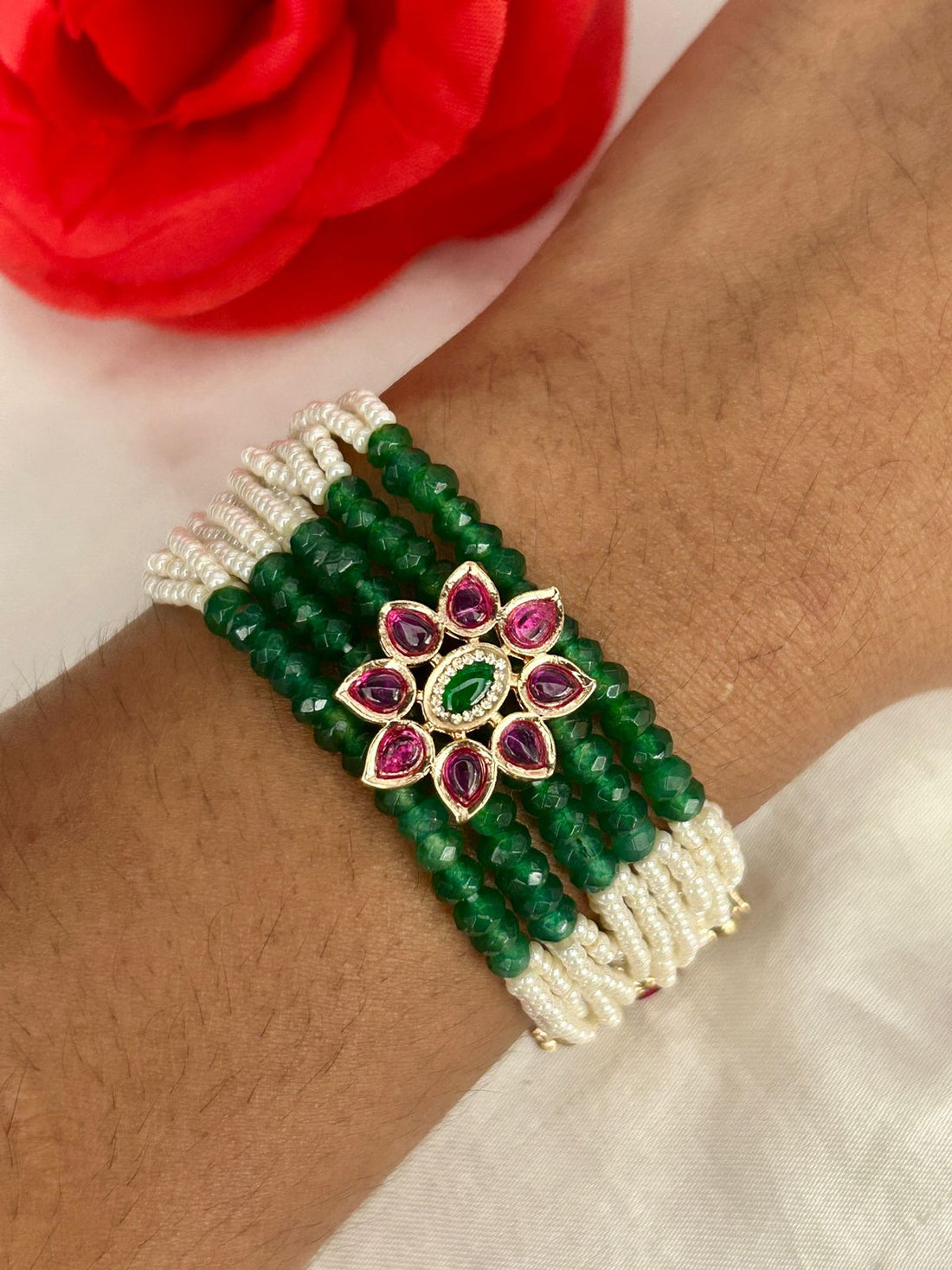 Green beaded bracelet with a floral design on a wrist, next to a red rose.