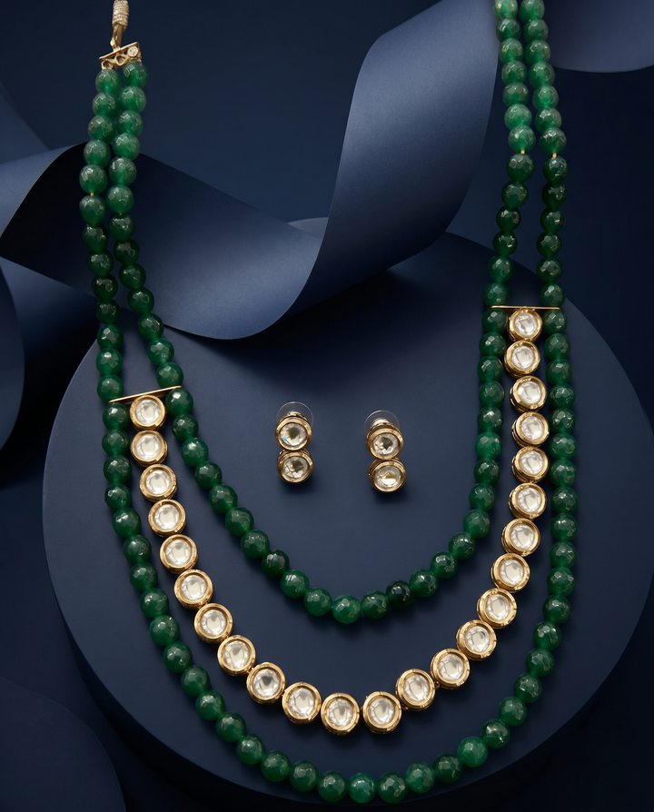 Green beaded necklace with gold accents and matching earrings on a dark blue background