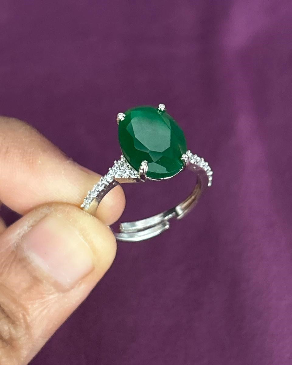Green gemstone ring held by a hand against a purple background