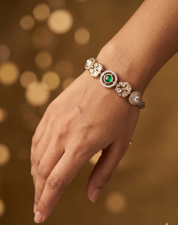 Hand wearing a decorative bracelet with a green gemstone against a warm, blurred background