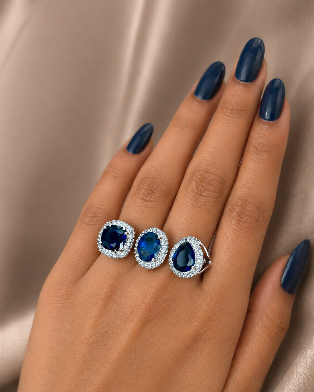 Hand wearing a ring and two earrings with blue gemstones on a neutral background