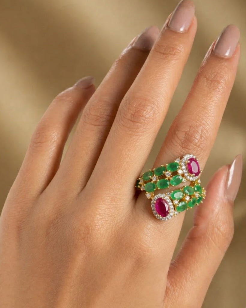 Hand wearing a ring with emeralds and rubies on a beige background