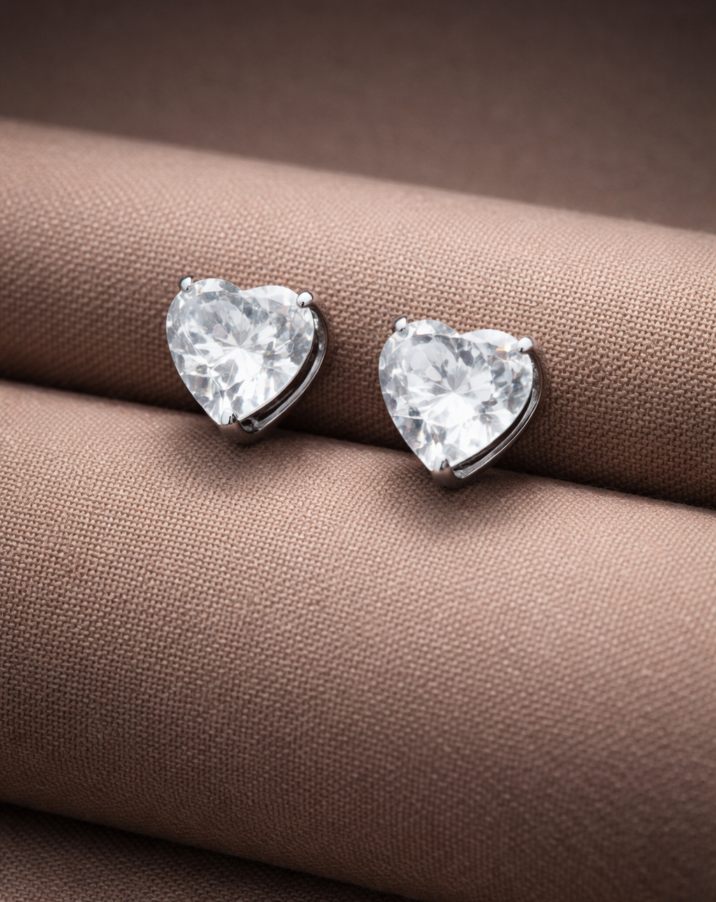 Heart-shaped diamond earrings on a brown fabric background