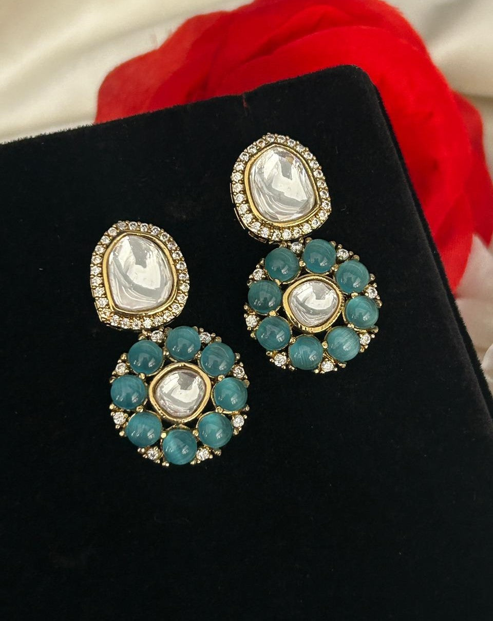 Jewelry earrings with turquoise stones and gold accents on a black stand.