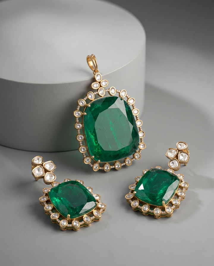 Jewelry set with emerald green stones and gold accents on a gray background