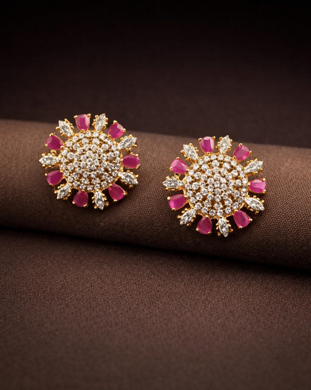 Pair of sun-shaped earrings with pink and clear stones on a brown surface
