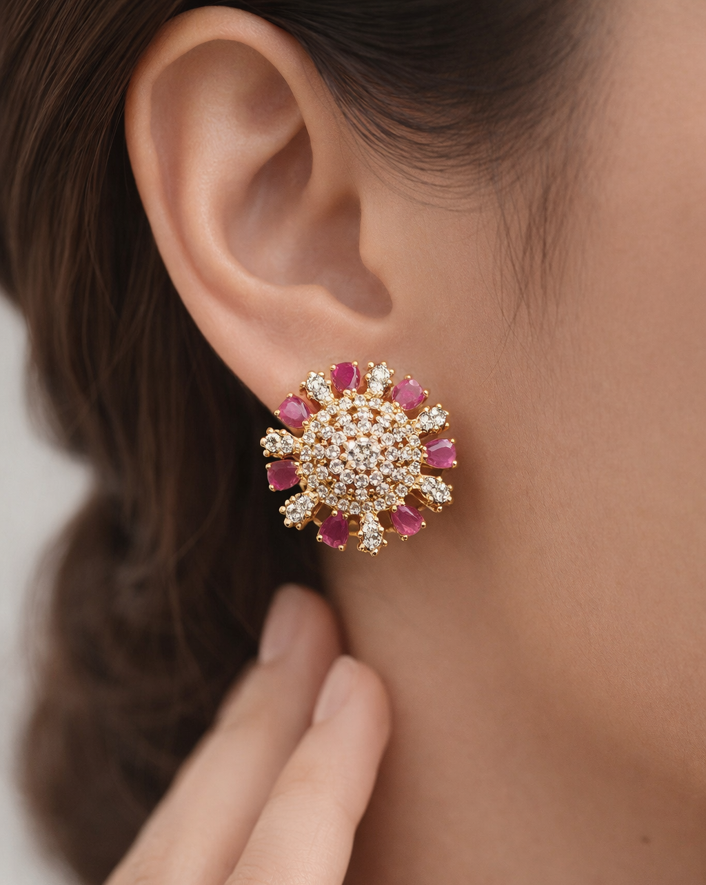 Close-up of a person wearing a gold and pink earrings with a blurred background