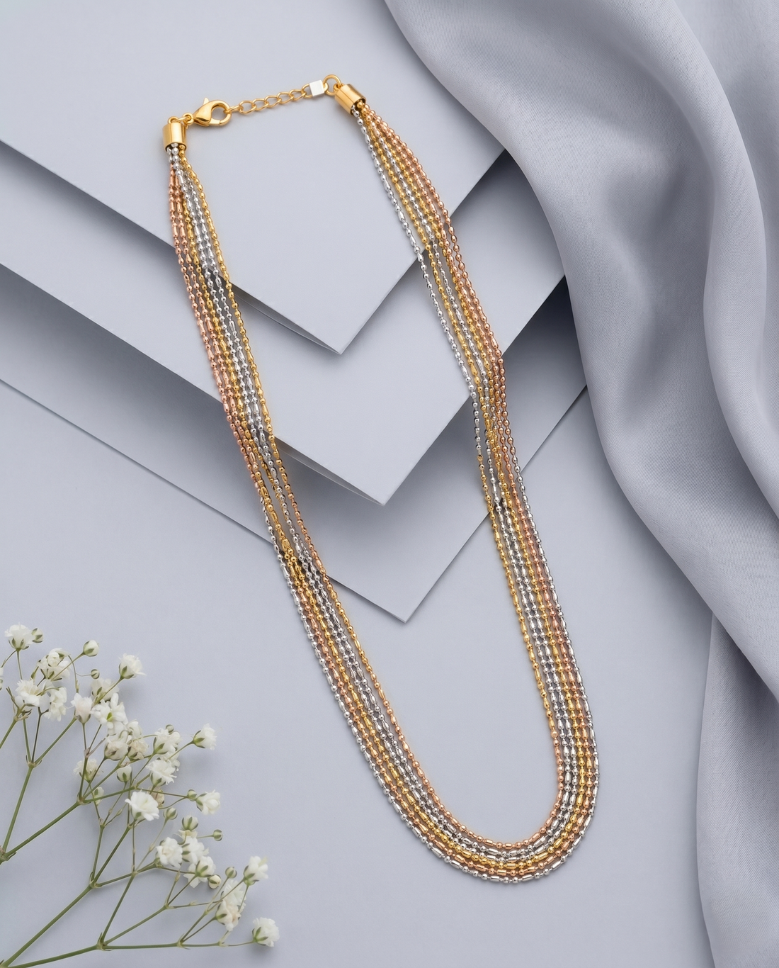 Multistrand beaded necklace with gold clasp on a light gray surface with white flowers.