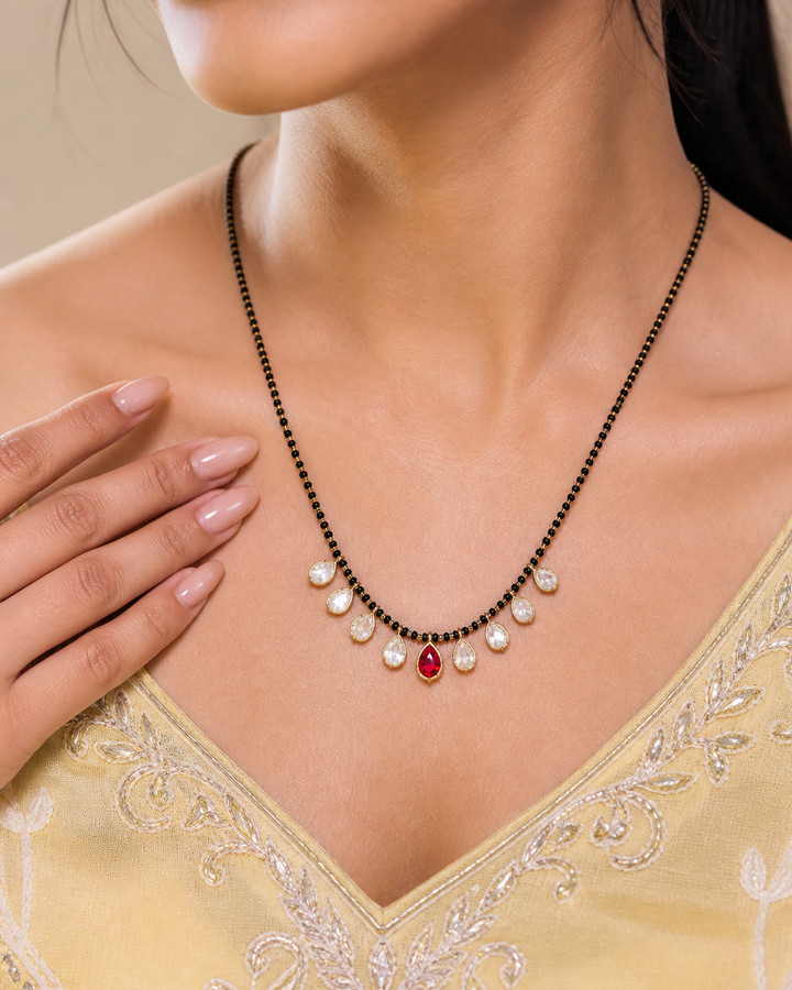 Necklace with pearls and a red gemstone on a person wearing a yellow embroidered garment.