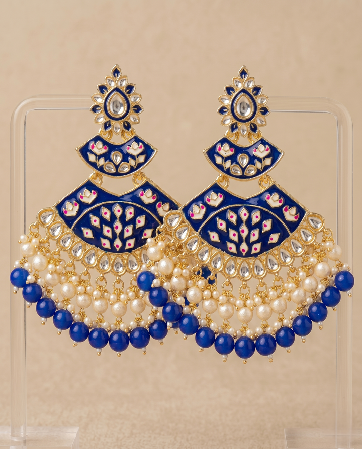Ornate earrings with blue and gold design on a beige background