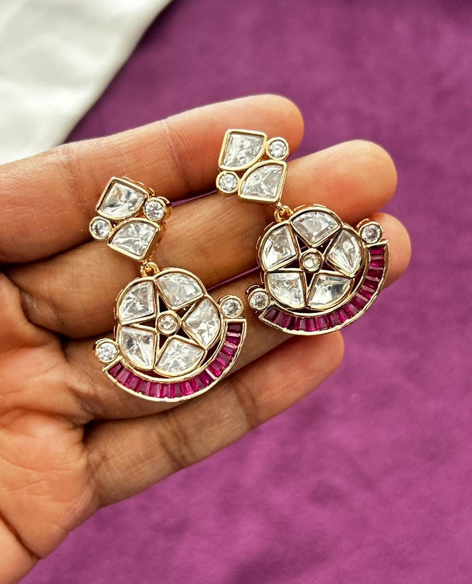 Ornate earrings with gemstones held in a hand against a purple background