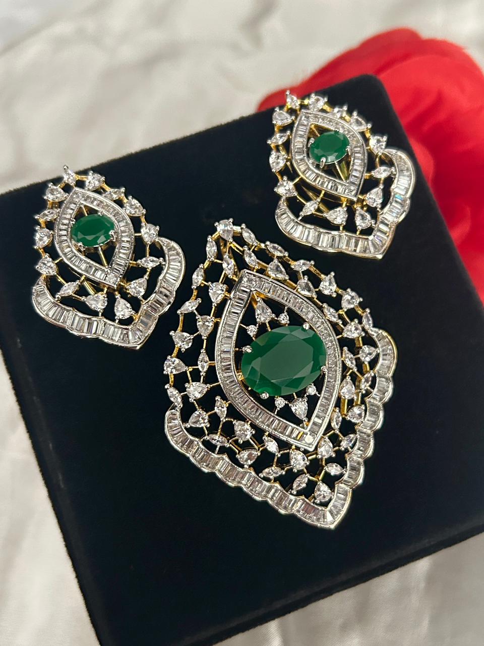 Ornate earrings with green gemstones on a black stand.