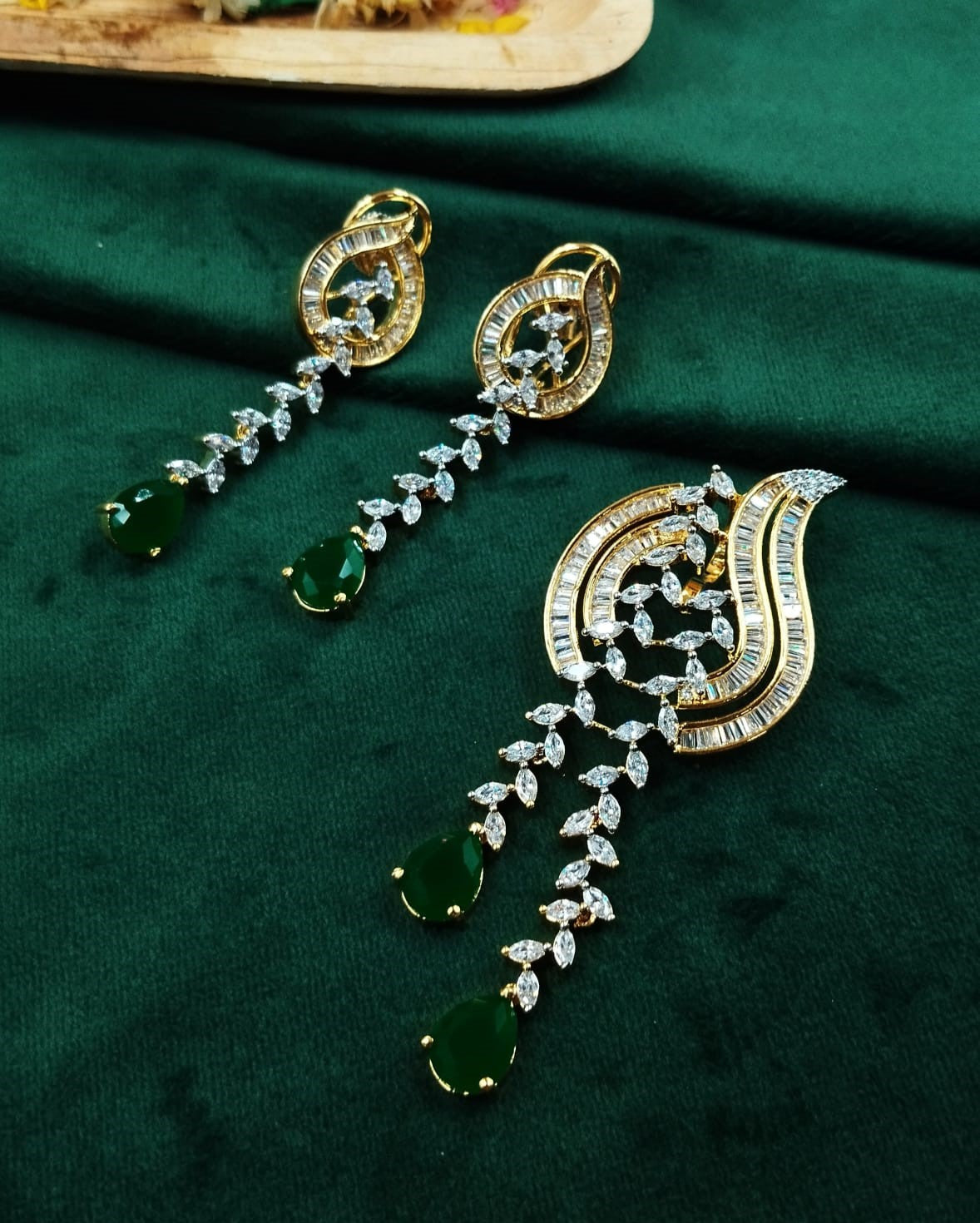 Ornate earrings with green gemstones on a dark green fabric background