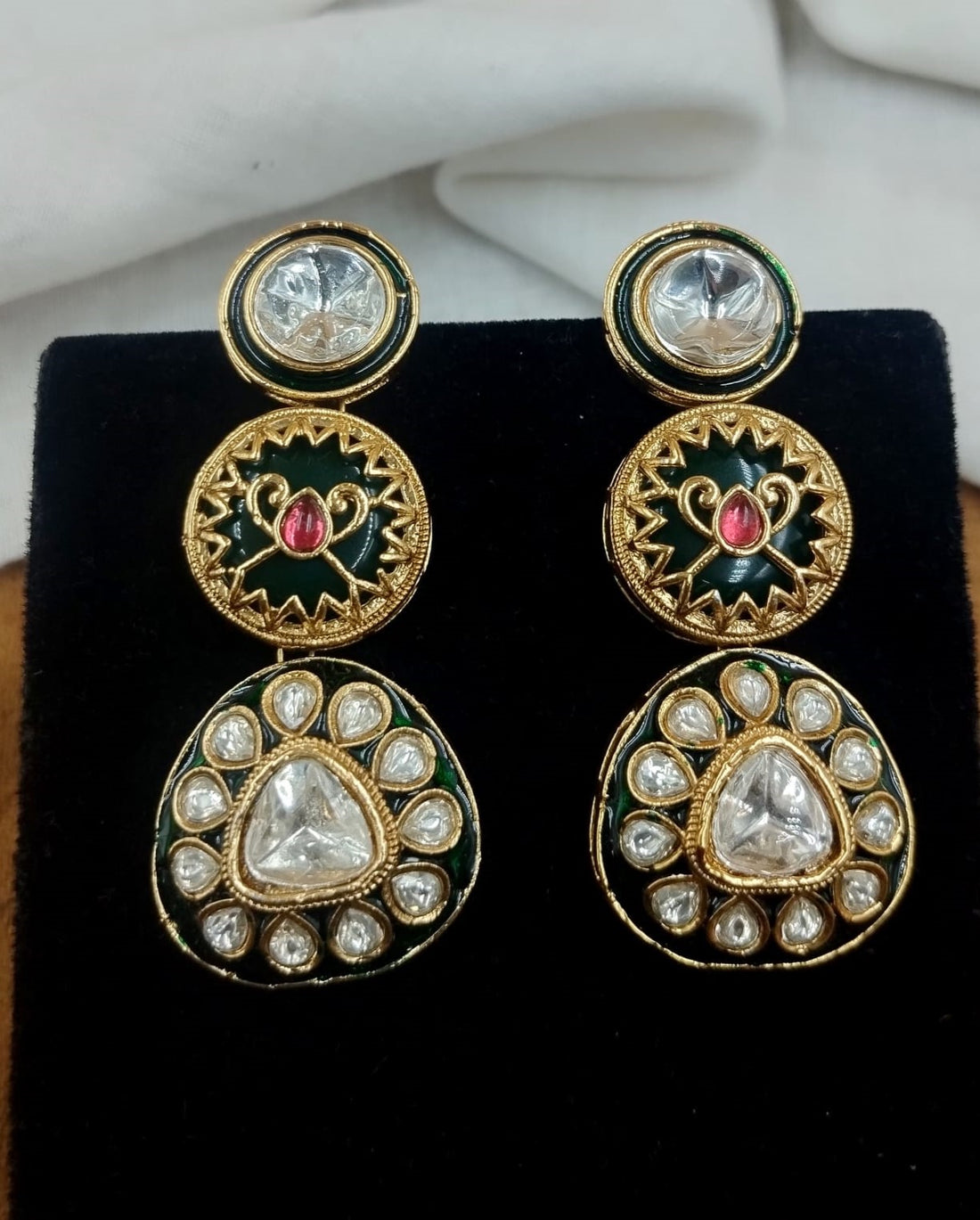 Close up view of polki kundan necklace with green and red enamel paired with matching earrings in gold finish