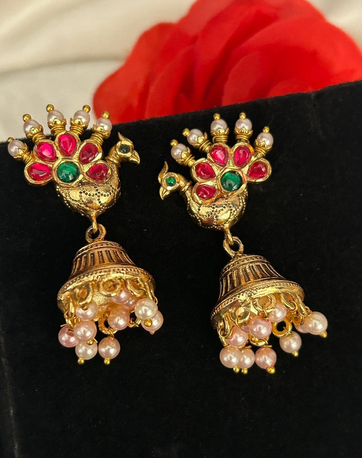 Ornate earrings with peacock design and pearl and gemstone details on a black background.