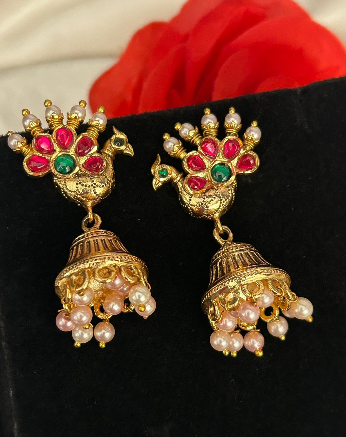 Ornate earrings with peacock design and pearl and gemstone details on a black background.