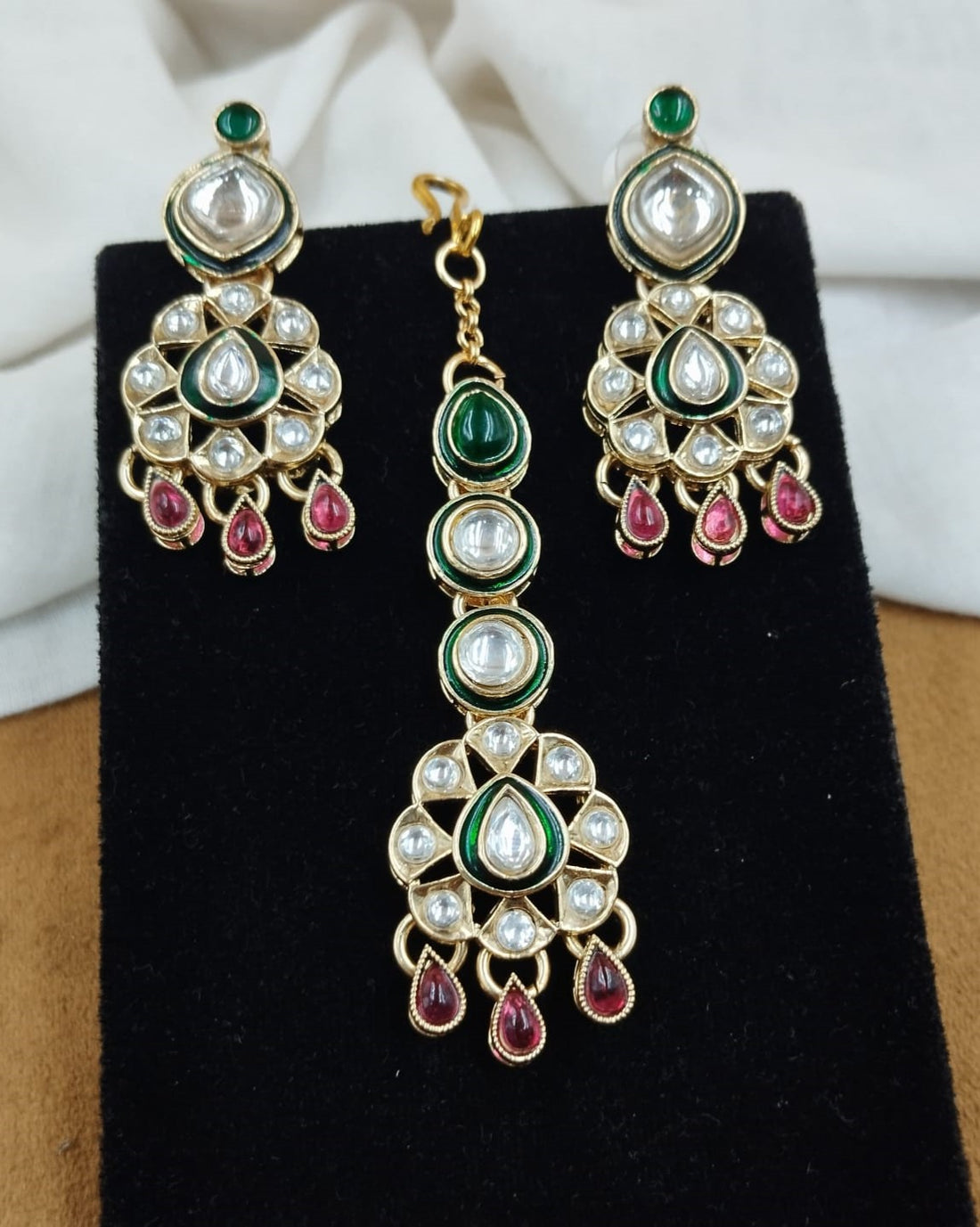 Close up view of polki kundan necklace with green and red enamel paired with matching earrings in gold finish