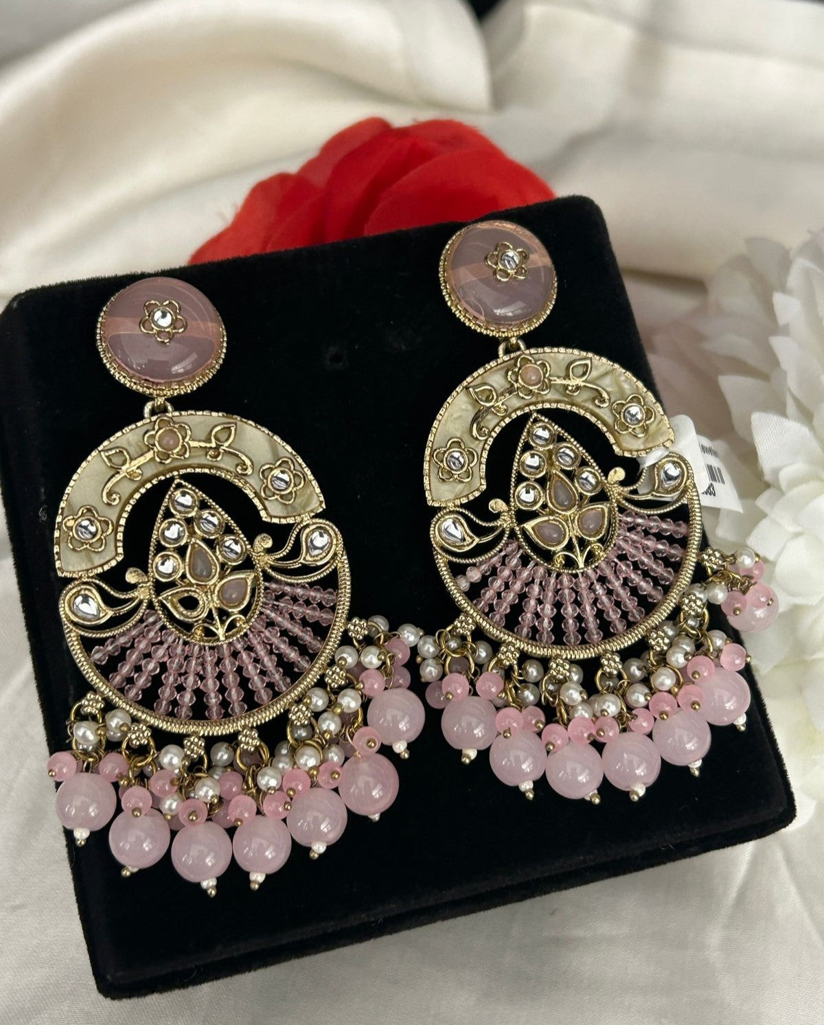 Ornate earrings with pink and gold details on a black stand.