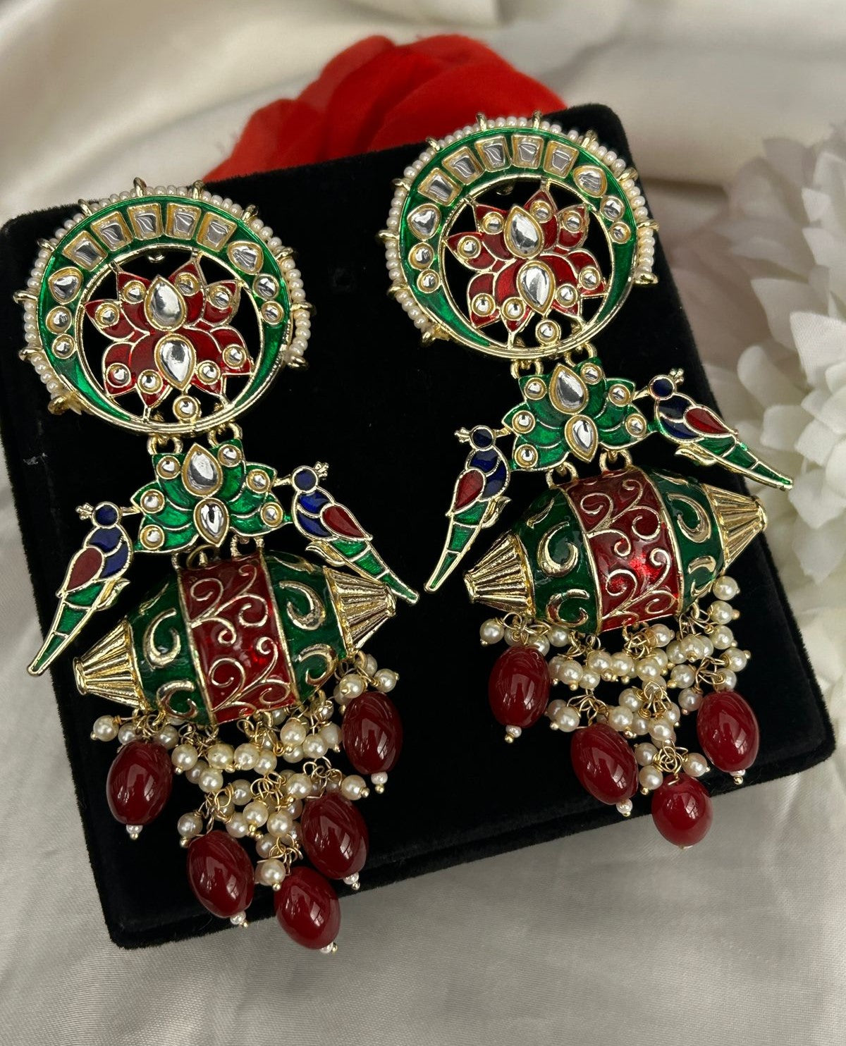 Ornate earrings with red and green colors on a black display stand.