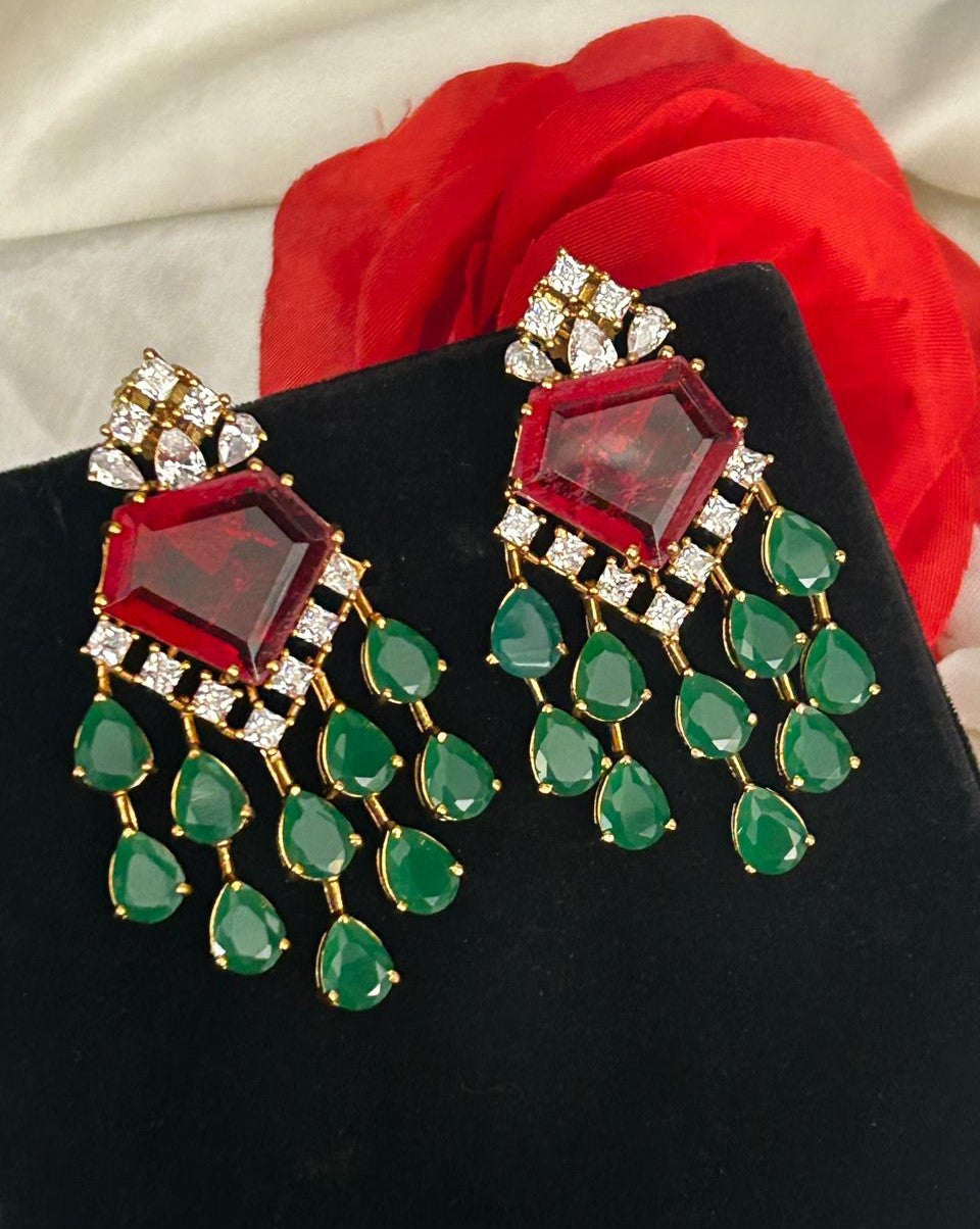 Ornate earrings with red and green gemstones on a black stand.